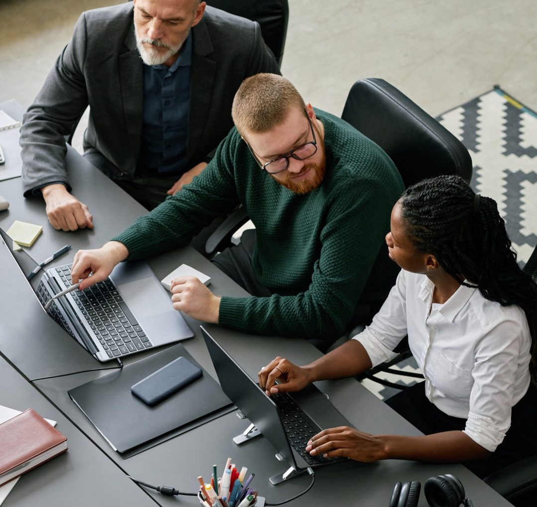 Collaborative Business Meeting with Diverse Team Group of business professionals discussing project strategy around conference table, with man pointing at laptop screen, engaging in productive discussion