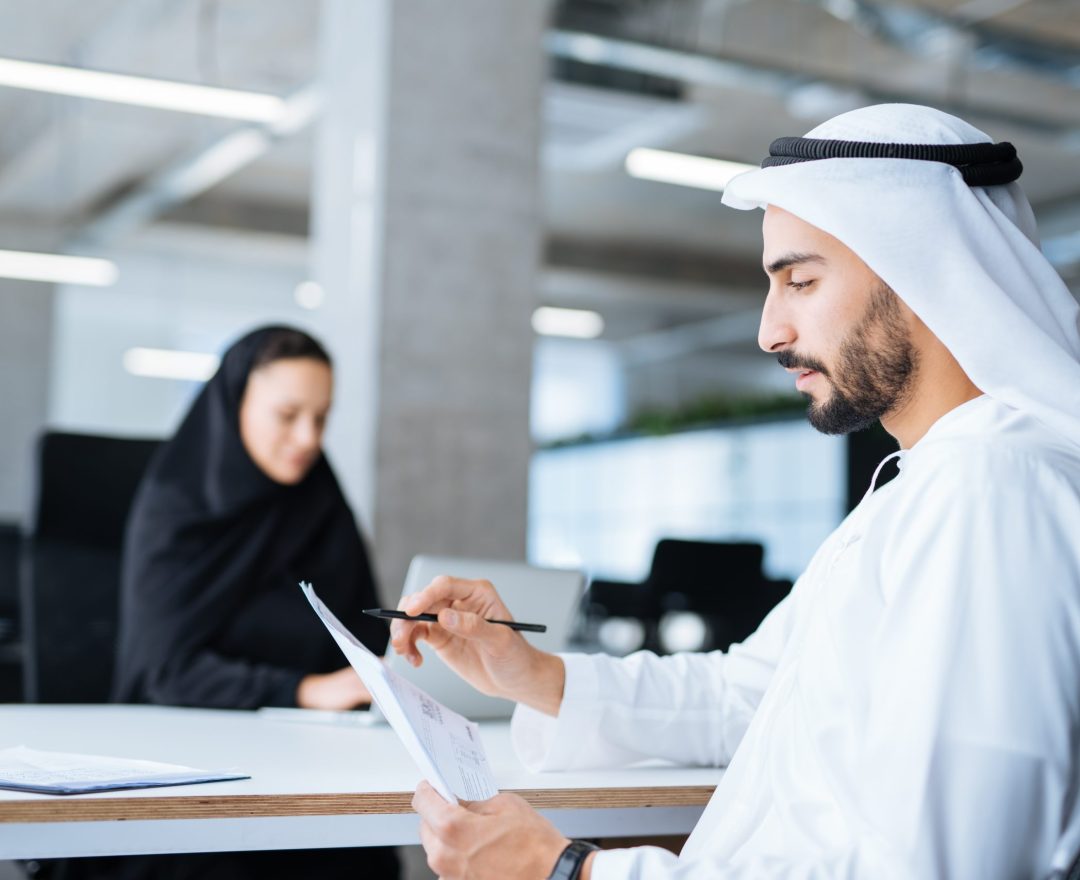 Man and woman with traditional clothes working in a business office of Dubai. Portraits of  successful entrepreneurs businessman and businesswoman in formal emirates outfits. Concept about middle eastern cultures, lifestyle and professional occupations