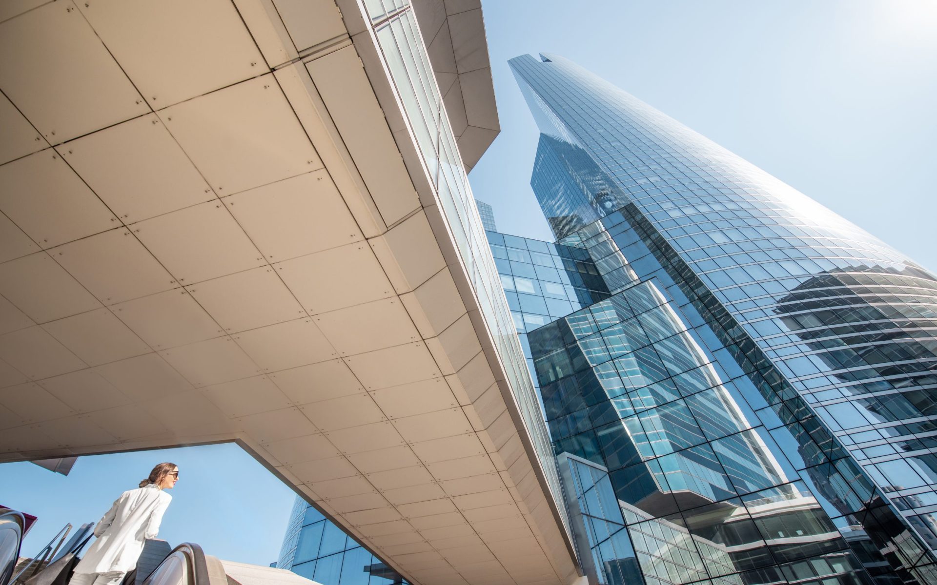 Geometrical view from below on the modern financial district with business woman going up on the escalator