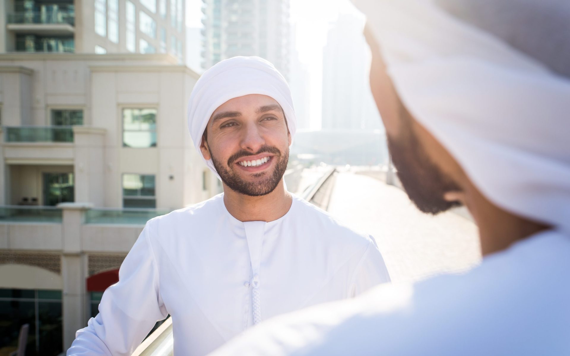 Middle-eastern young adults wearing kandora walking outdoors in Dubai - Two businessmen meeting outdoors